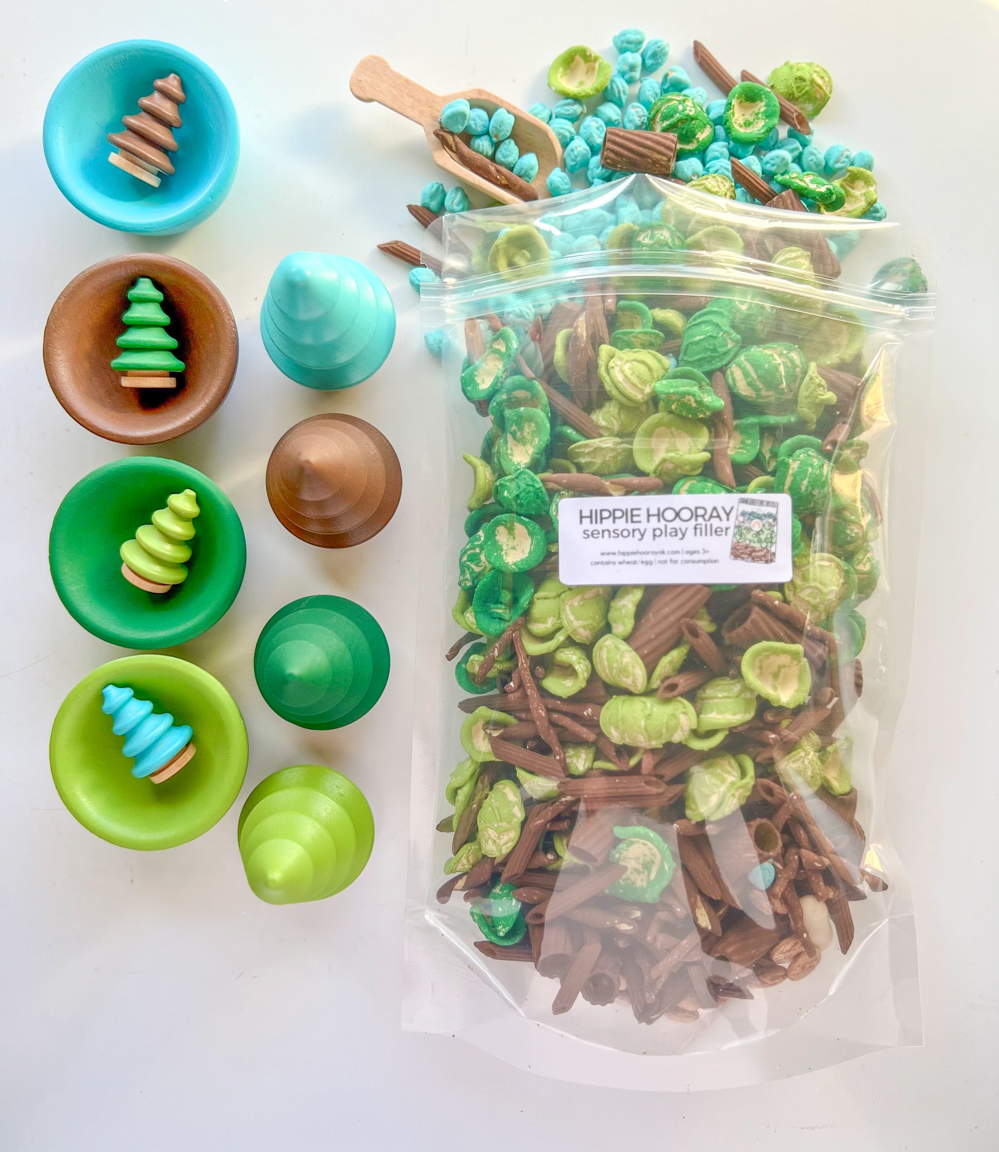 A variety of colorful pasta and sensory bin fillers displayed in bowls and a clear bag, with wooden accessories used for sensory play.